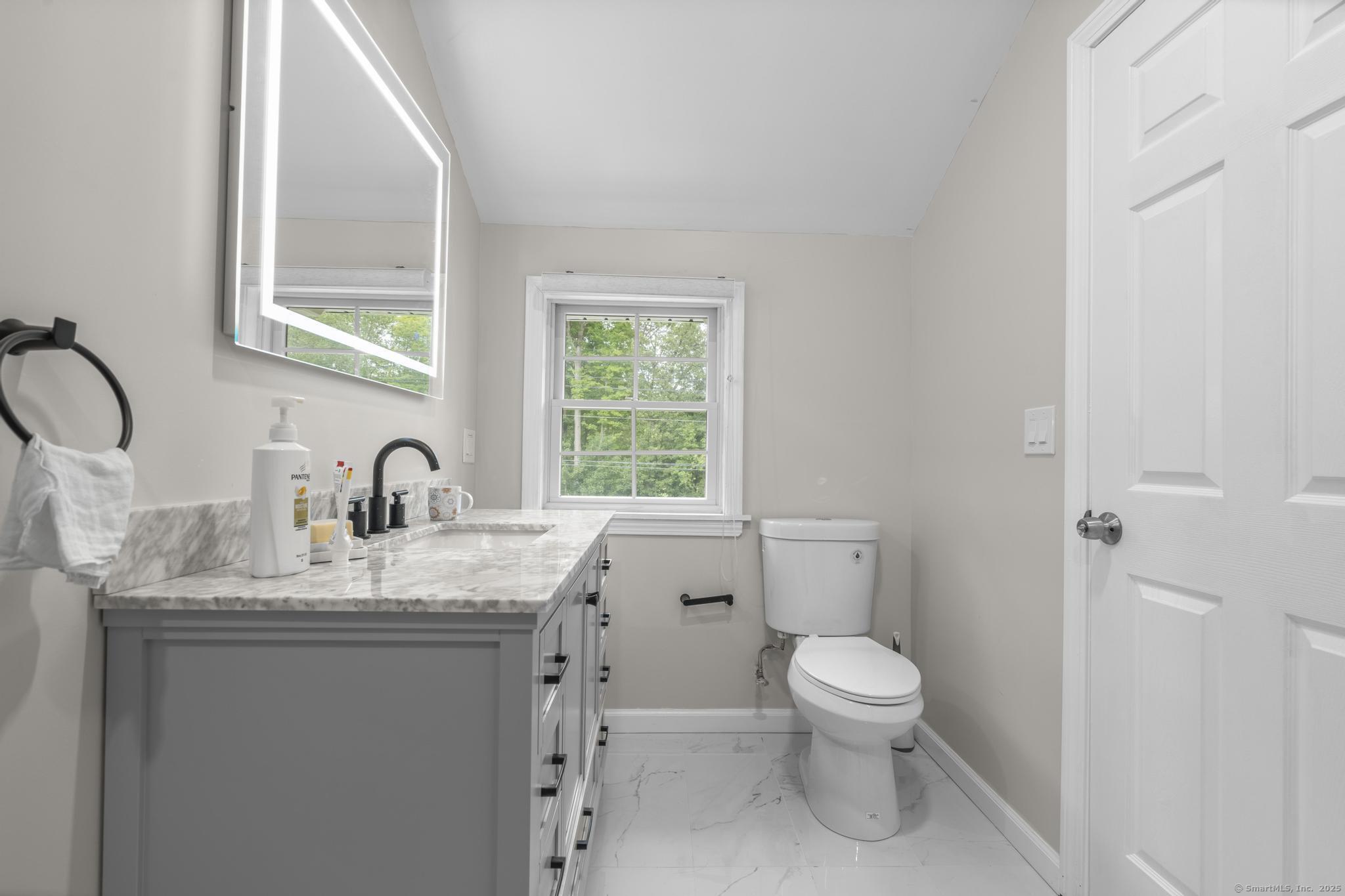 424 Racebrook Road Orange, CT 06477 - Photo 22 of 36 a bathroom with a granite countertop toilet a sink a mirror and a window