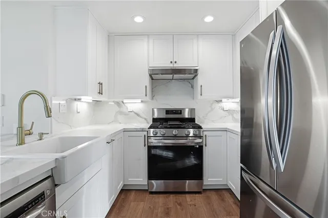 a kitchen with stainless steel appliances granite countertop a stove a refrigerator and a sink with wooden floor