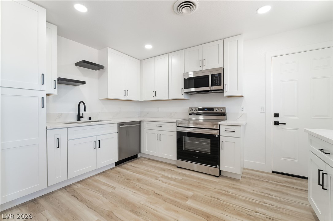 39 Lowery Street Henderson, NV 89015 - Photo 11 of 40 A well-lit, contemporary kitchen showcasing sleek white cabinetry and natural wood-look flooring.