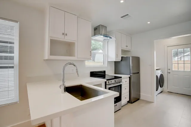 a kitchen with stainless steel appliances a stove a refrigerator sink and white cabinets with wooden floor