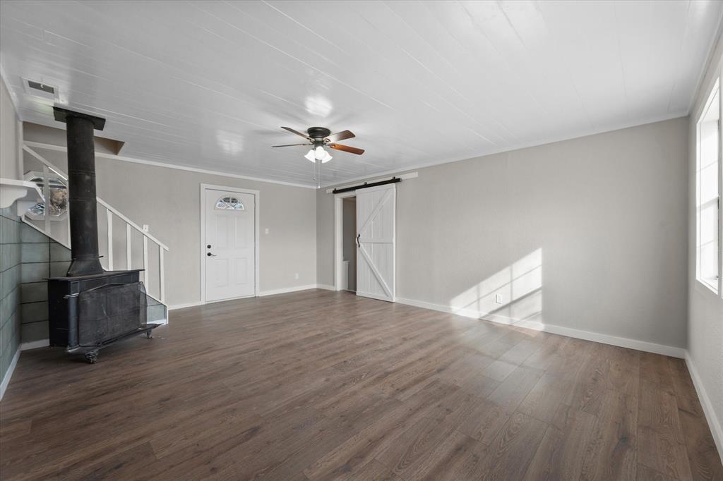 443 County Road 3799 Springtown, TX 76082 - Photo 15 of 33 Unfurnished living room with a wood stove, a barn door, dark wood-style flooring, ceiling fan, and ornamental molding