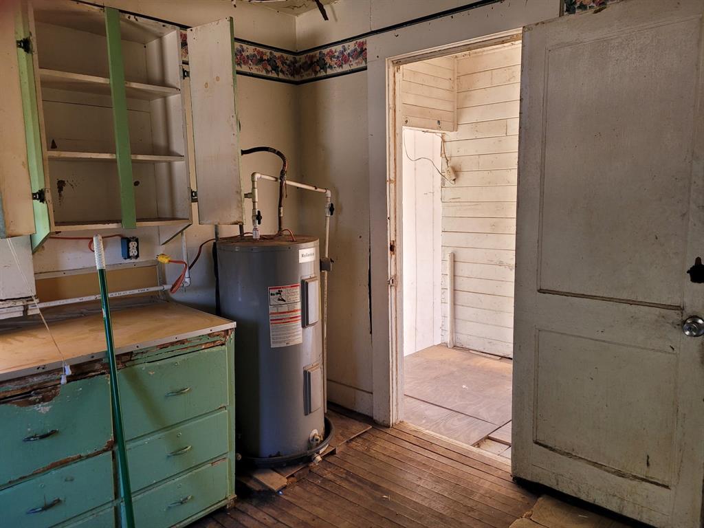 909 Ivan Road Waco, TX 76706 - Photo 7 of 10 Room featuring a built-in water heater, painted cabinetry, and wood-finish flooring