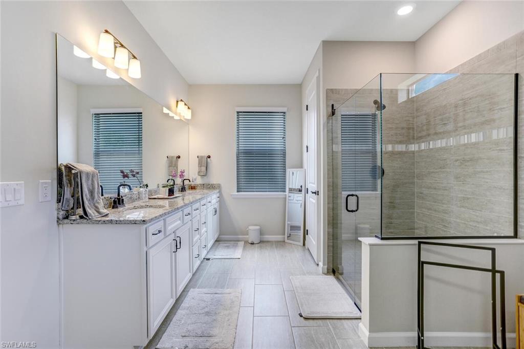 19809 Beechcrest Place Estero, FL 33928 - Photo 13 of 33 a large bathroom with a double vanity sink a mirror and a shower