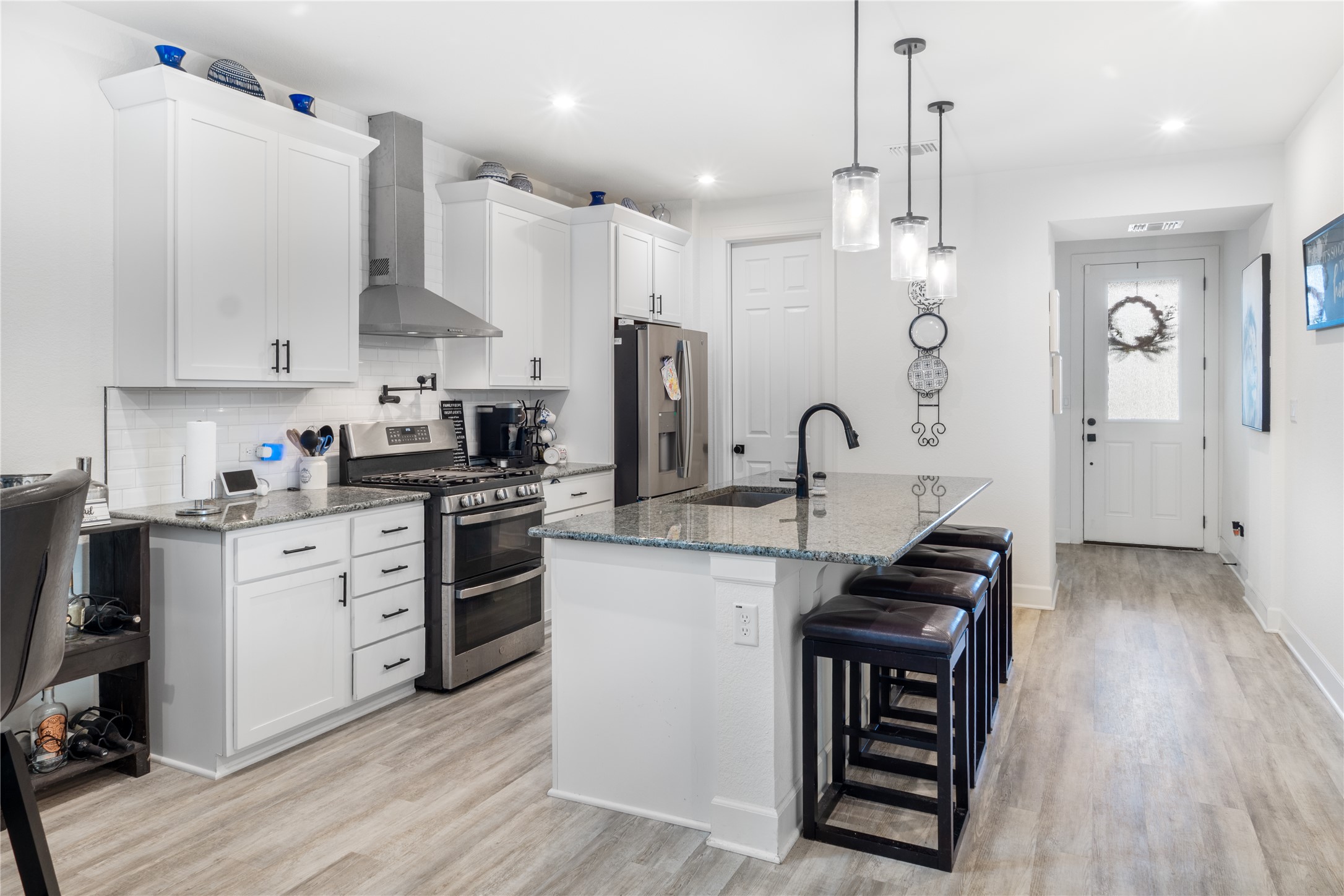 20811 Phebe Foster Street Manor, TX 78653 - Photo 8 of 40 Kitchen featuring stainless steel appliances, a kitchen bar, light stone countertops, white cabinetry, and light wood-style flooring