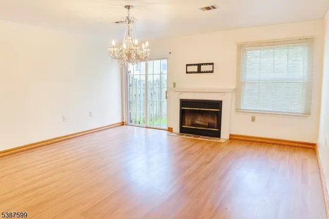 a view of an empty room with wooden floor fireplace and a window
