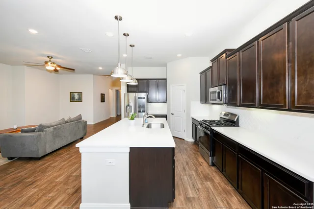 a large kitchen with kitchen island a stove a sink dishwasher a dining table and chairs with wooden floor