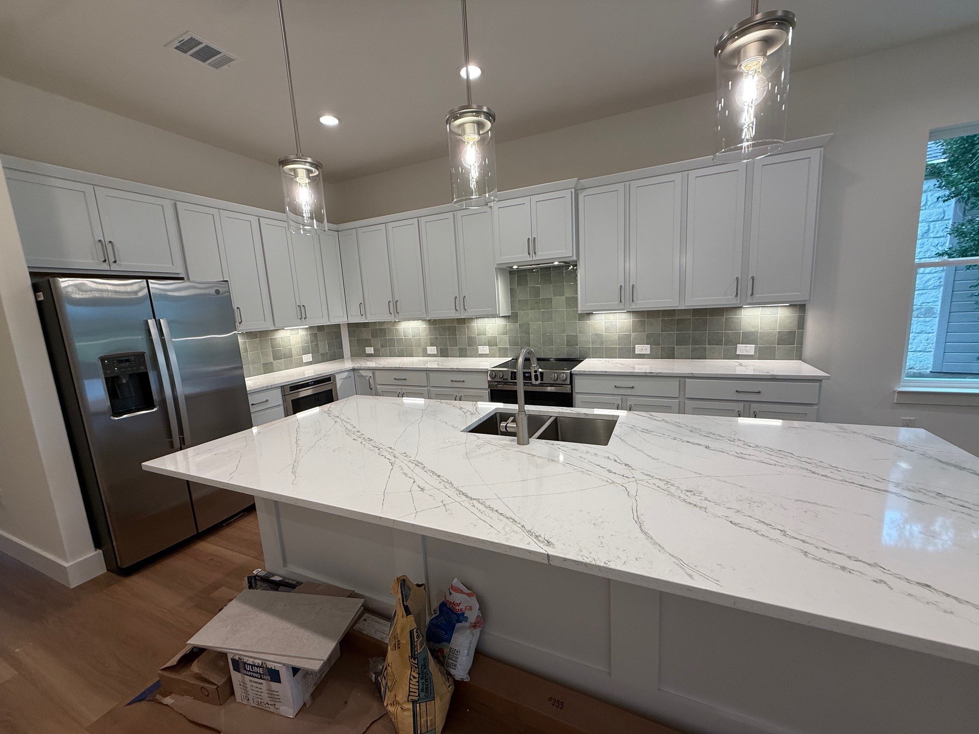 110 Firestone Place Meadowlakes, TX 78654 - Photo 4 of 18 Spacious kitchen featuring a large island with a waterfall-edge countertop, stainless steel appliances, extensive light-toned cabinetry, a mosaic tile backsplash, and recessed and pendant lighting
