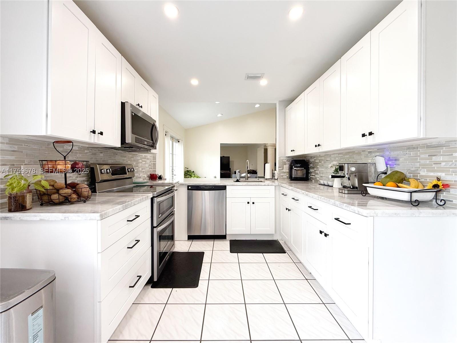 20520 Southwest 124th Place Miami, FL 33177 - Photo 24 of 34 a kitchen with stainless steel appliances kitchen island granite countertop a refrigerator sink stove and white cabinets