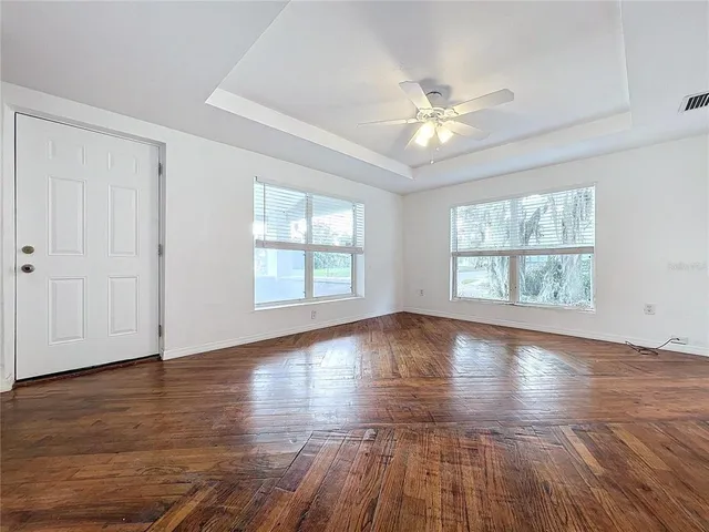 an empty room with wooden floor chandelier fan and windows