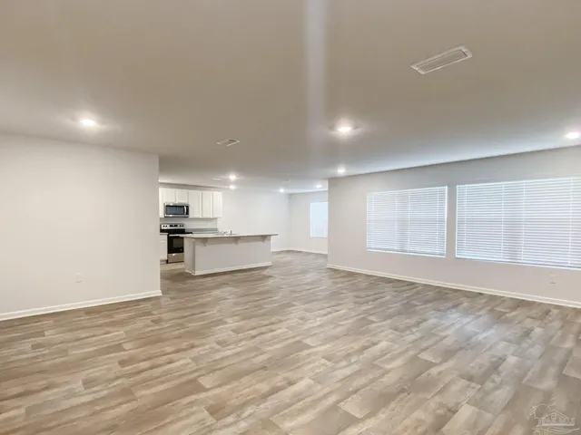 a view of empty room with wooden floor and kitchen
