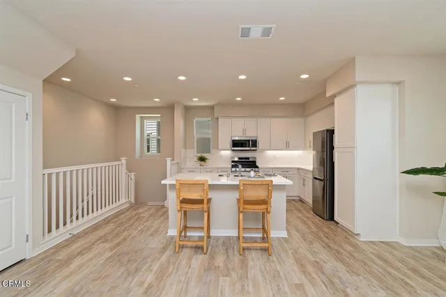a kitchen with stainless steel appliances kitchen island granite countertop a dining table chairs and white refrigerator