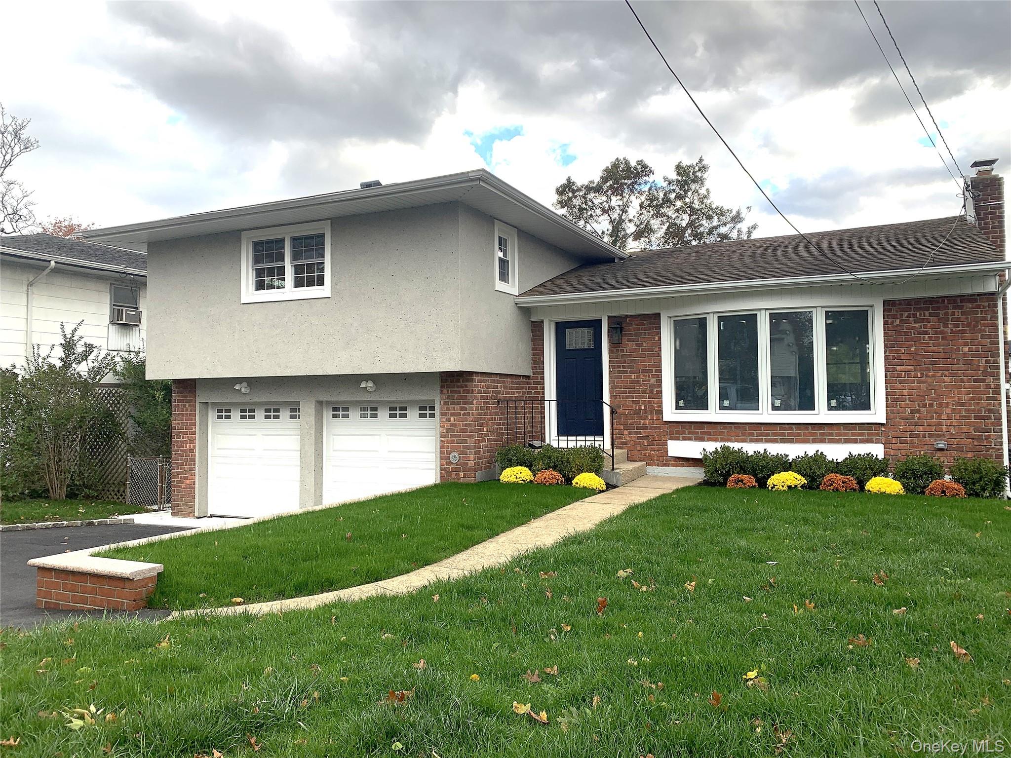 Split level home with brick siding, a front yard, an attached garage, and driveway