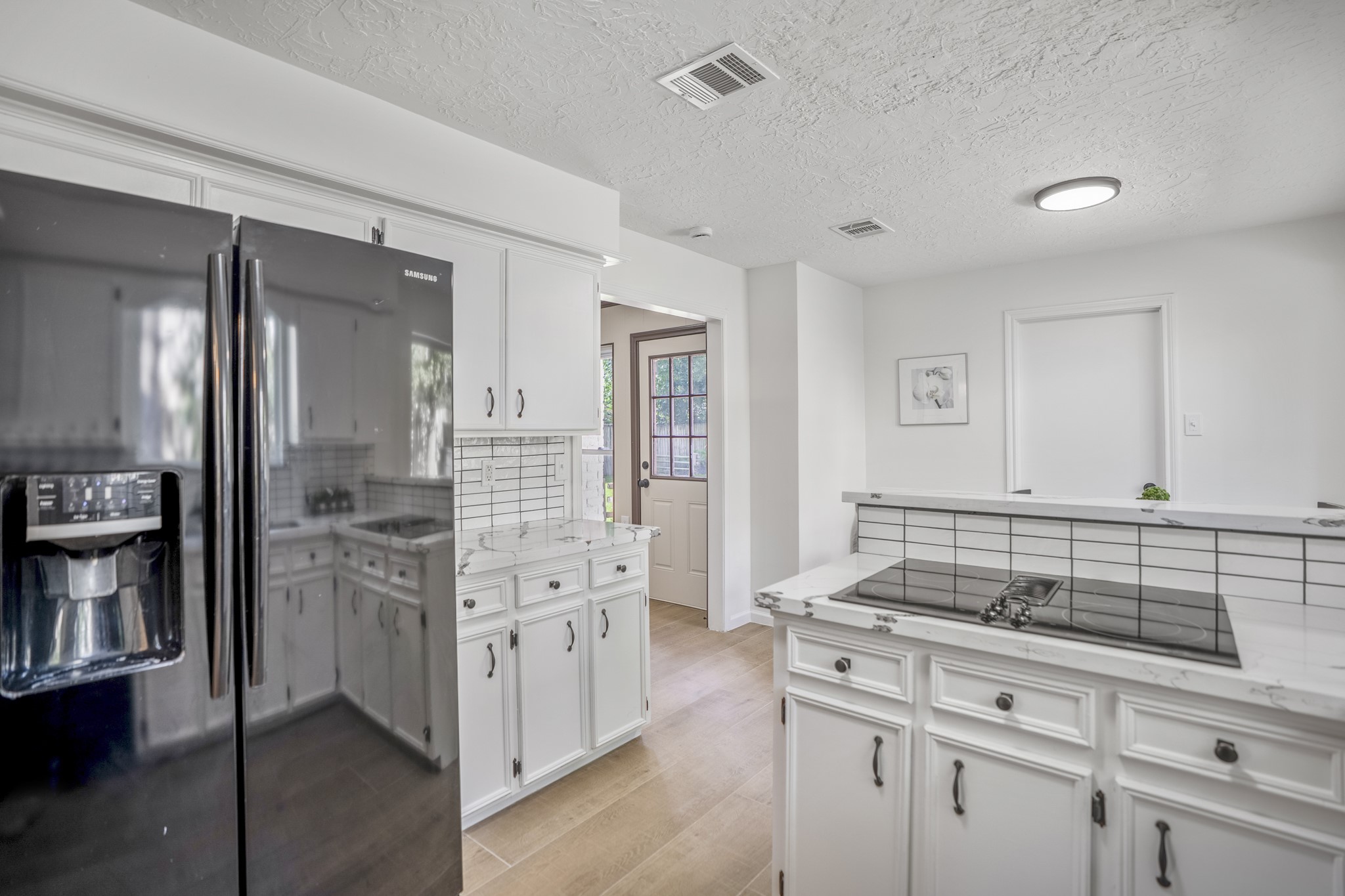 6303 Larkmount Drive Spring, TX 77389 - Photo 13 of 50 Turning toward the opposite side of the kitchen, even more counter space and storage come into view beyond the refrigerator, helping the layout feel both functional and well organized. The glass cooktop sits right at the raised breakfast bar, keeping whoever’s cooking connected to the breakfast area just beyond, while the doorway past the cabinetry loops back around to the family room located at the rear of the home.