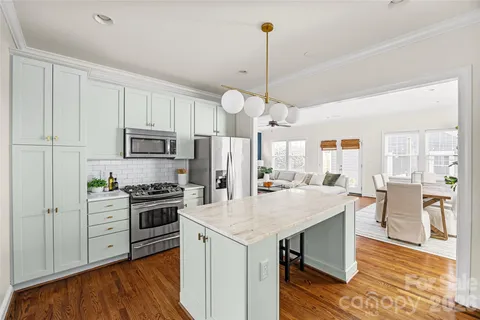 a open kitchen with stainless steel appliances granite countertop a stove refrigerator and white cabinets with wooden floor