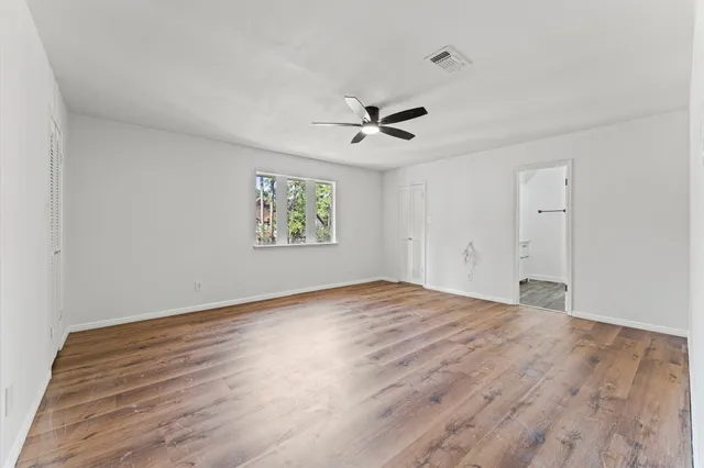 an empty room with wooden floor ceiling fan and windows