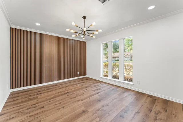an empty room with wooden floor chandelier fan and windows