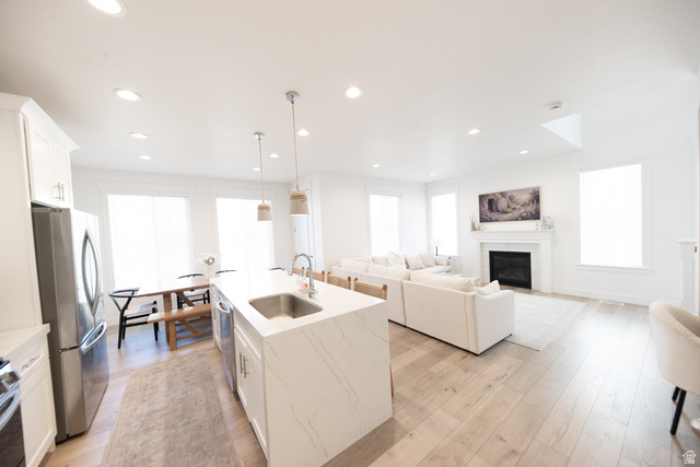 1404 East Rustic Wood Court Sandy, UT 84092 - Photo 5 of 33 Open-concept living space featuring wood-finish flooring, a kitchen island with a stainless steel sink, recessed lighting, a fireplace with a mantel, and multiple windows