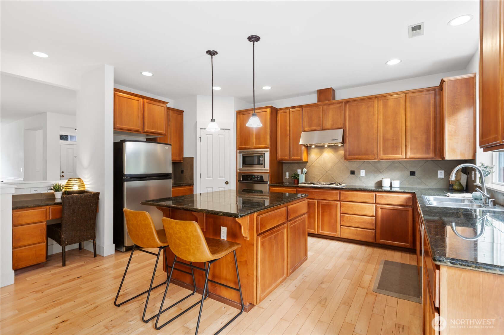 22829 36th Avenue Southeast Bothell, WA 98021 - Photo 12 of 39 a kitchen with stainless steel appliances granite countertop wooden cabinets a refrigerator a sink a stove and chairs with wooden floor
