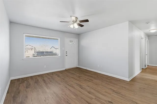 an empty room with wooden floor chandelier fan and windows