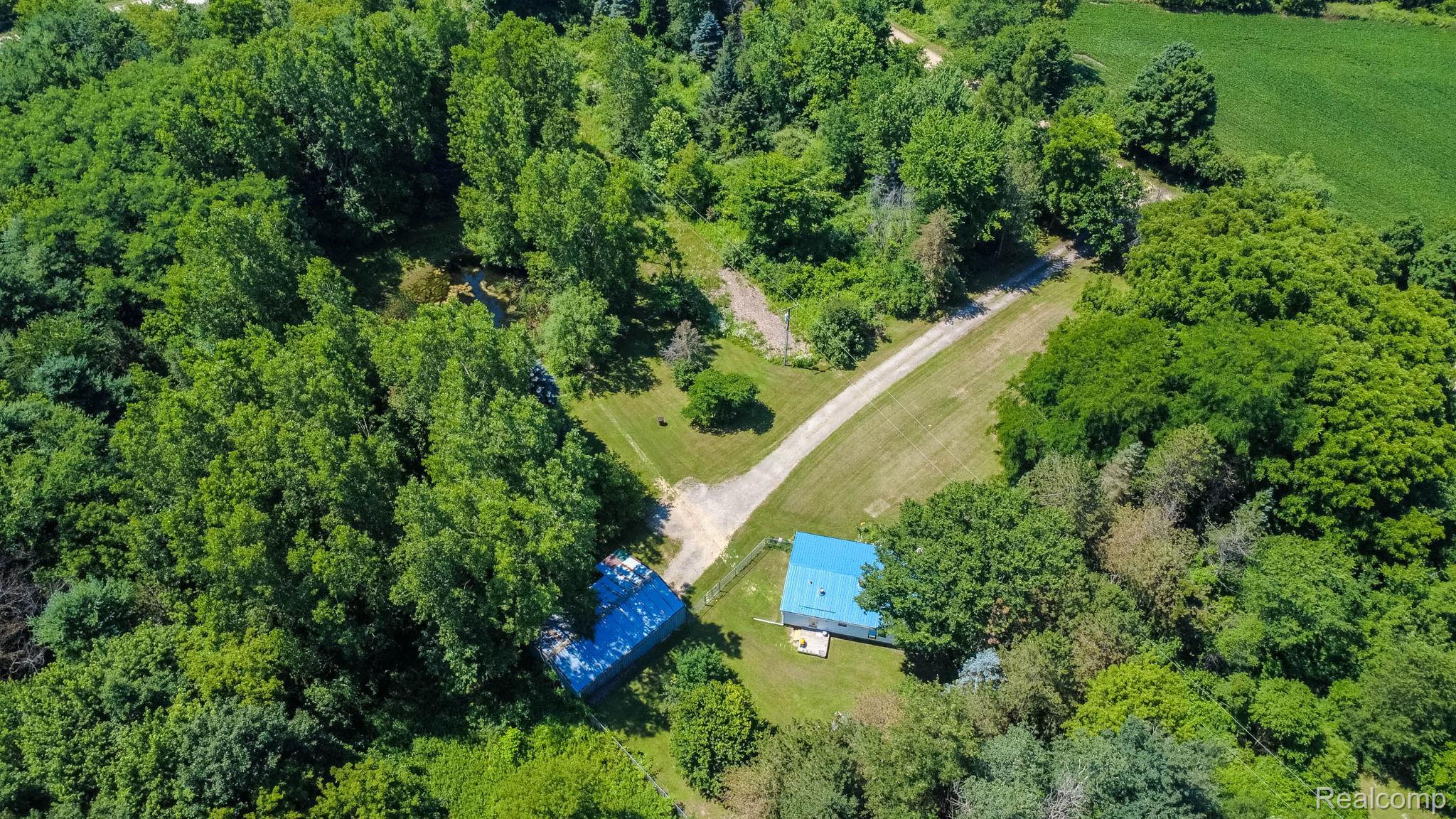 38 South Force Road Attica, MI 48412 - Photo 47 of 53 Expansive wooded property featuring two structures with blue roofs, a gravel driveway, and surrounding green clearings