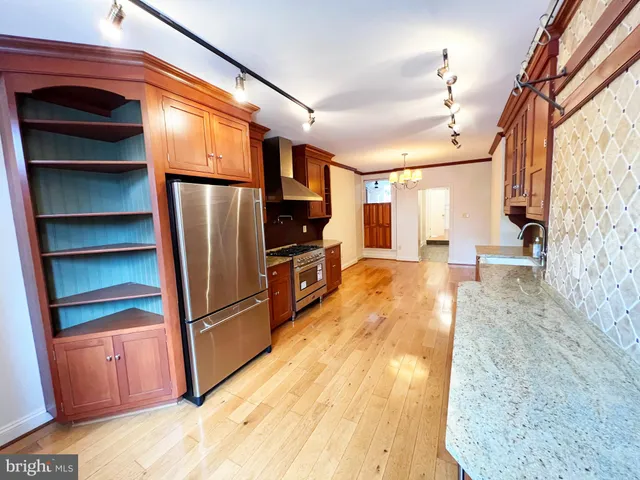 a kitchen with stainless steel appliances kitchen island granite countertop a refrigerator a stove and a sink with wooden floor