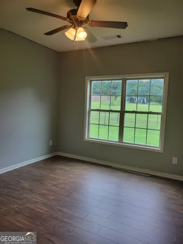 an empty room with wooden floor fan and windows