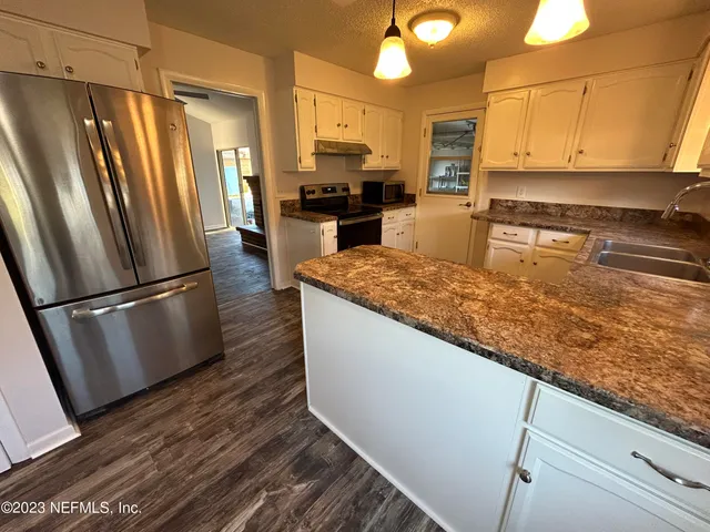 a kitchen with stainless steel appliances granite countertop a refrigerator a stove and a sink with wooden floor