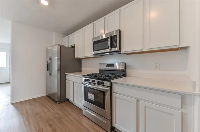 a kitchen with stainless steel appliances granite countertop white cabinets a stove a microwave and a refrigerator