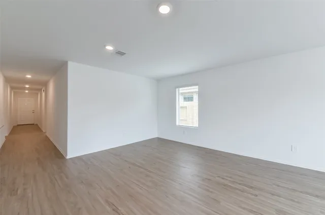 a view of an empty room with wooden floor and window
