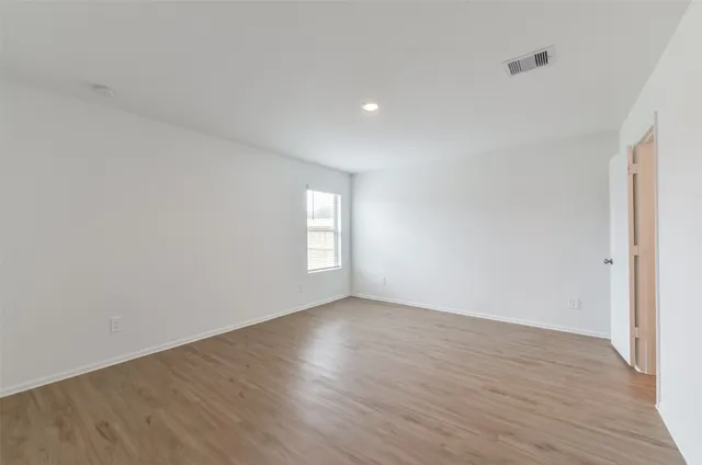 a view of an empty room with wooden floor and a kitchen