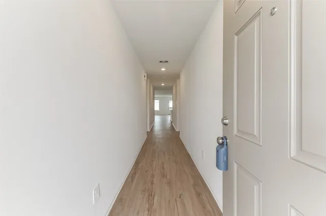 a view of a hallway with wooden floor and a bathroom