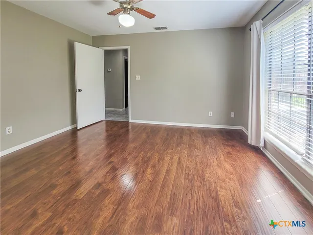 a view of an empty room with wooden floor and a window