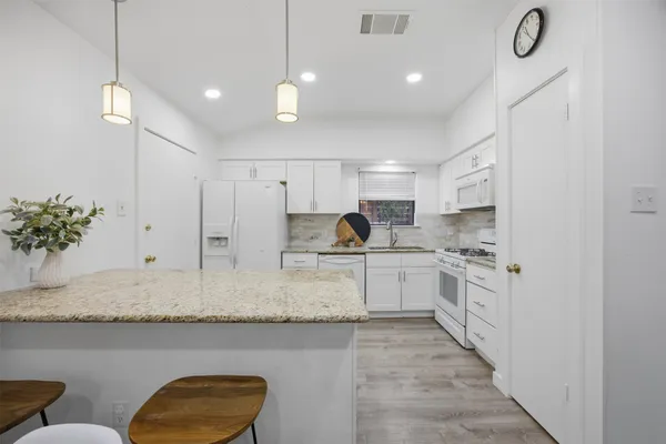 a large white kitchen with stainless steel appliances granite countertop a stove a sink a refrigerator and a dining table with wooden floor