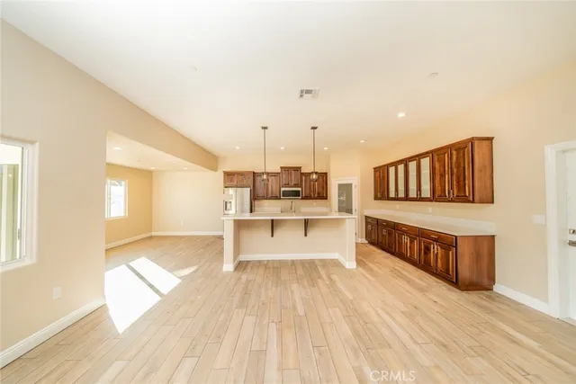 a living room with stainless steel appliances kitchen island granite countertop a refrigerator a sink dishwasher a stove and a dining table with wooden floor