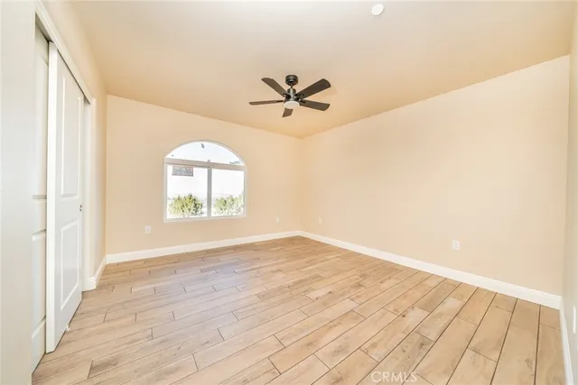 an empty room with wooden floor ceiling fan and windows