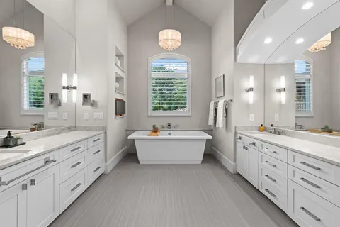 a spacious bathroom with double vanity a mirror a bathtub and a window