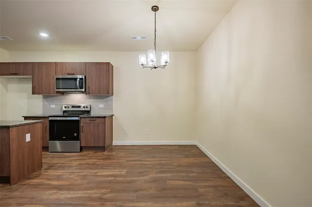 a kitchen with stainless steel appliances granite countertop a stove a sink dishwasher a refrigerator and a dining table with wooden floor