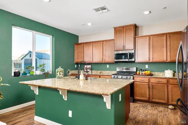 a kitchen with kitchen island granite countertop a sink a stove cabinets counter space and a window