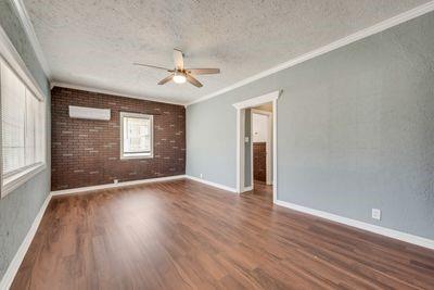 930 Freeman Street Sherman, TX 75092 - Photo 3 of 18 Expansive room featuring wood-finish flooring, a brick accent wall, and a ceiling fan with integrated lighting