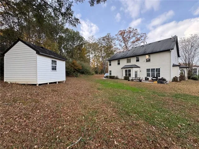 a view of a white house that has a small yard and large trees