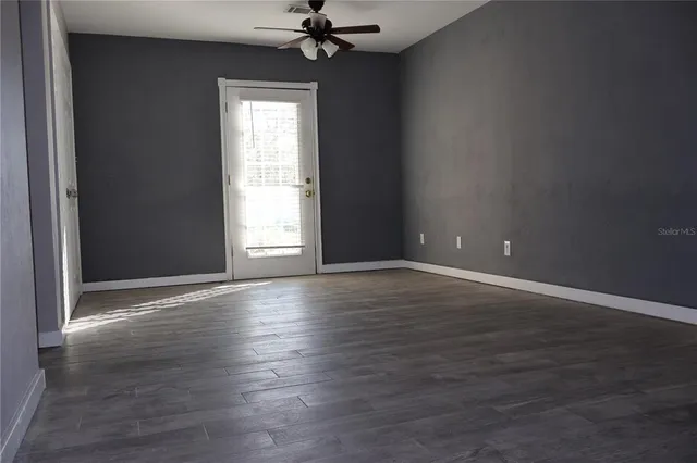 an empty room with wooden floor chandelier fan and windows