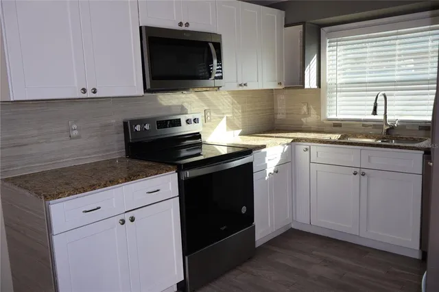 a kitchen with granite countertop white cabinets and a stove with wooden floor