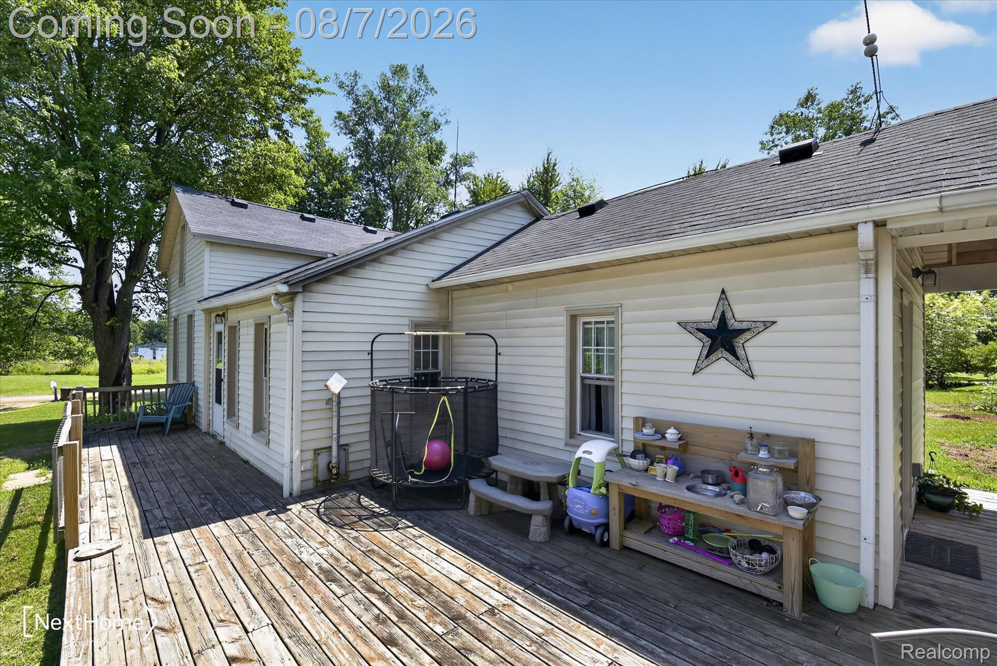 23740 Carleton West Road Belleville, MI 48111 - Photo 4 of 58 Charming cottage-style home featuring a spacious composite deck with mature shade trees, board-and-batten siding exterior, decorative star accent, and convenient single-story layout
