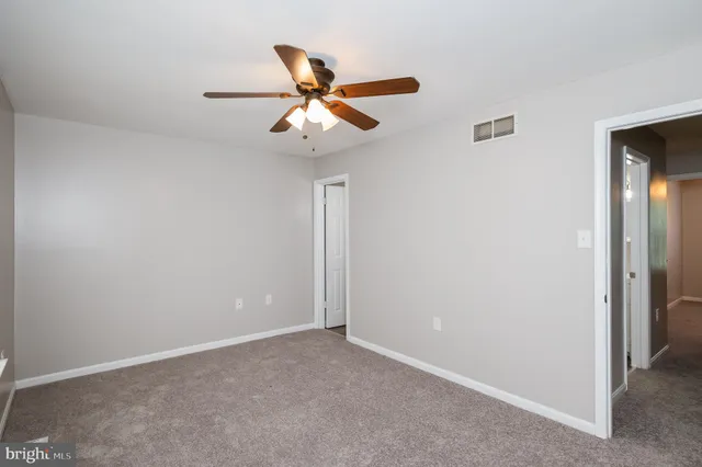a view of an empty room with wooden floor and a ceiling fan
