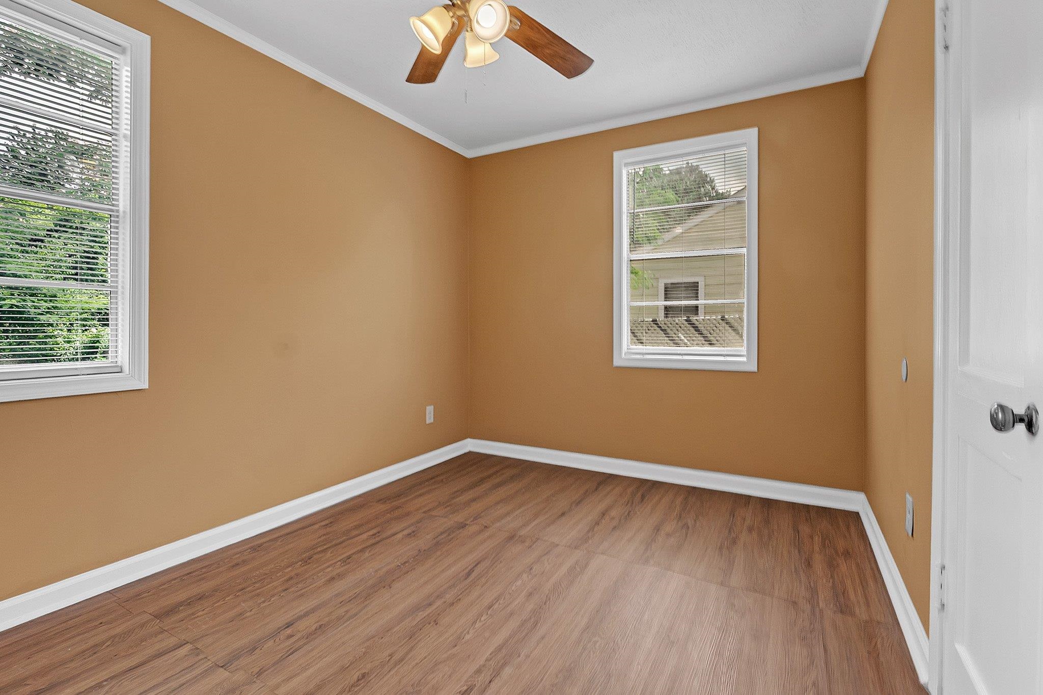3186 Alta Road Memphis, TN 38109 - Photo 12 of 14 Room featuring wood-finish flooring, two windows with blinds, a ceiling fan with integrated lighting, white baseboards, and a white door with dark hardware