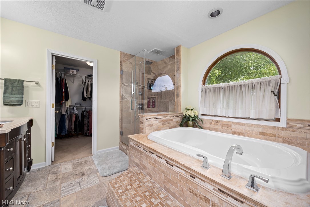 3270 North Ridge Road Vermilion, OH 44089 - Photo 32 of 49 Built-in soaking tub with chrome fixtures, arched window, walk-in shower with glass enclosure, beige tiled flooring, and a walk-in closet with built-in shelving