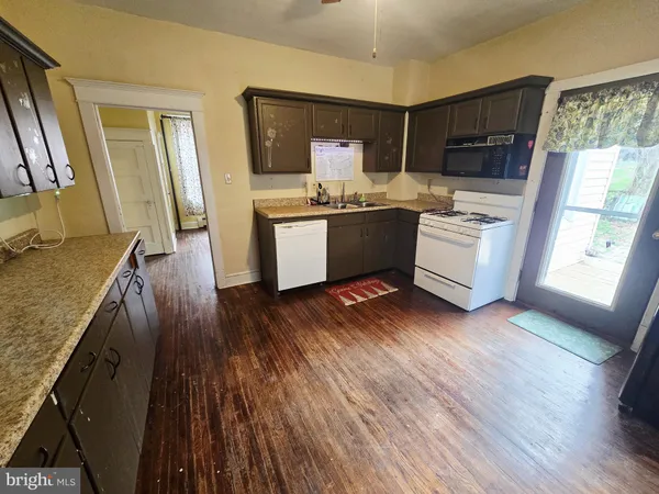 a kitchen with granite countertop a stove a sink a refrigerator wooden floor and cabinets