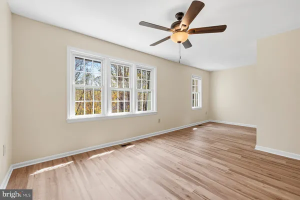 an empty room with wooden floor fan and windows