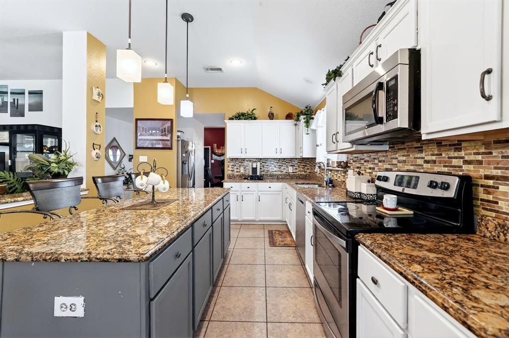 511 Chestnut Trail Forney, TX 75126 - Photo 13 of 32 Spacious kitchen featuring a large island with pendant lighting, white upper and lower cabinetry, stone-look countertops, and a mosaic tile backsplash