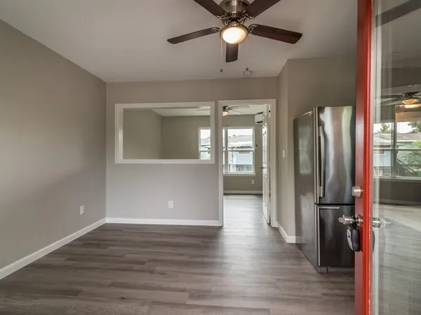 an empty room with wooden floor and way to kitchen